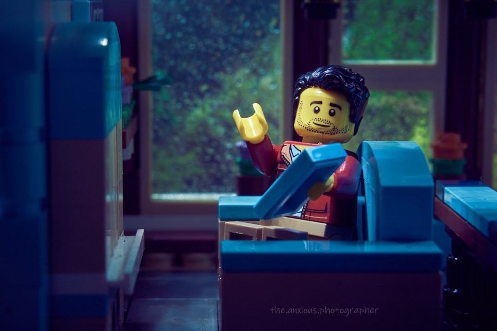 Lego man with dark hair sits in a chair, it rains outside