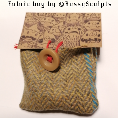 Fabric bag with a button has a cardboard flap decorated by a drawing of goblin faces.